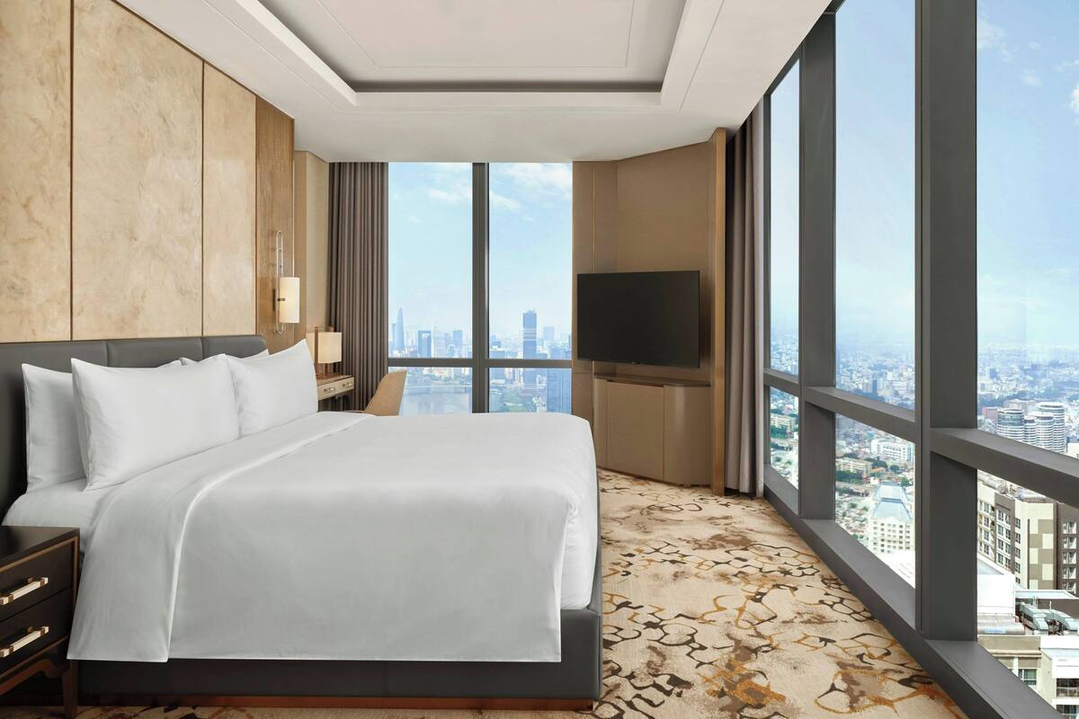 Habitación de hotel con una cama grande, televisión y vista a la ciudad.