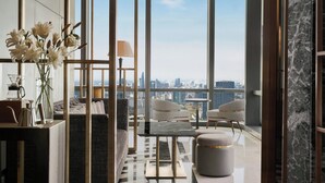 Una sala de estar moderna con vista a la ciudad, que incluye un sofá, sillones, una mesa de centro y un jarrón con flores.