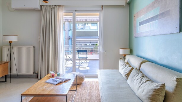 Een moderne kamer met een bank, een salontafel en uitzicht door een schuifdeur op een buitenruimte met een stoel en tafel.