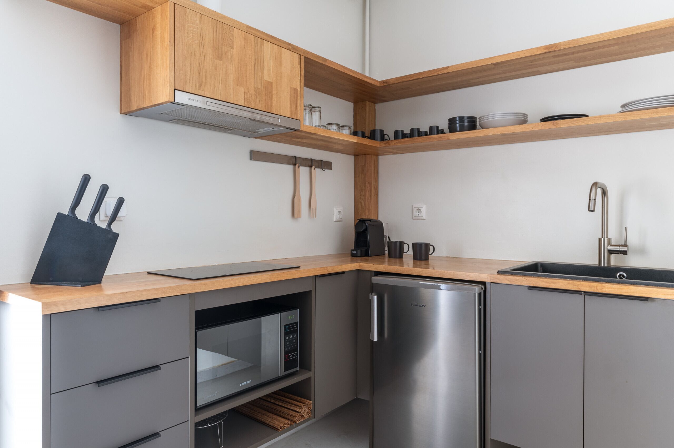 Uma cozinha moderna com prateleiras de madeira, forno embutido, geladeira e pia.