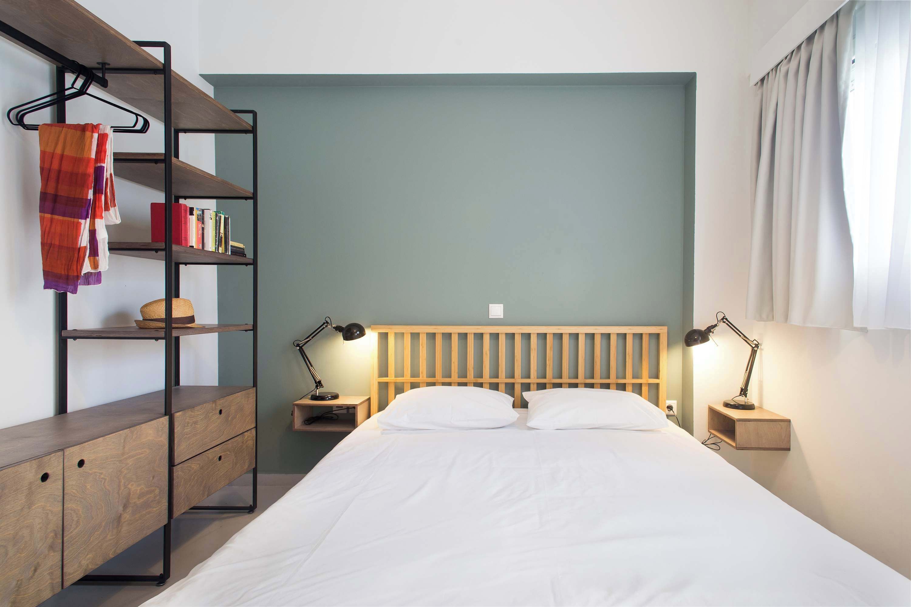 A bedroom with a bed, two bedside tables with lamps, a wooden headboard, a bookshelf, and a hanging towel.