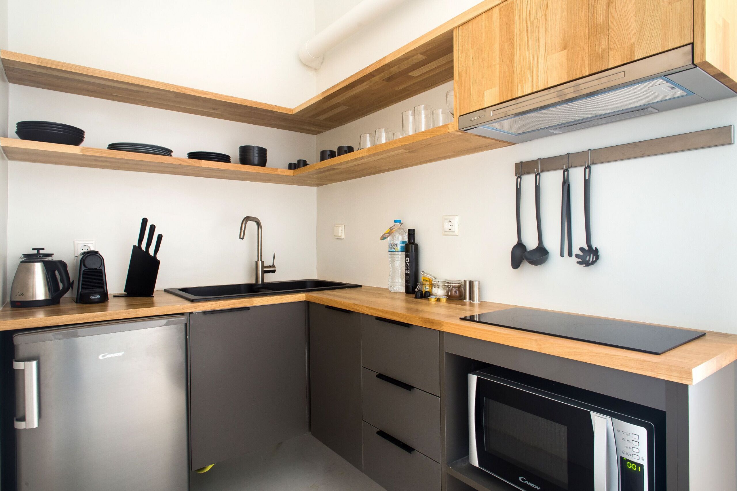 A modern kitchen with stainless steel appliances, wooden shelves, and hanging utensils.