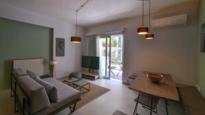 Een moderne woonkamer met een bank, salontafel en een eettafel. Er is een televisie, een lamp en een raam met uitzicht op het omliggende landschap.