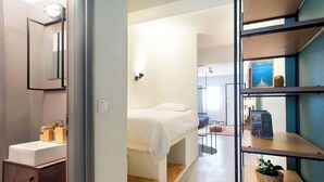 Een moderne slaapkamer met een bed, nachtkastje, spiegel en plank met boeken en een plant.
