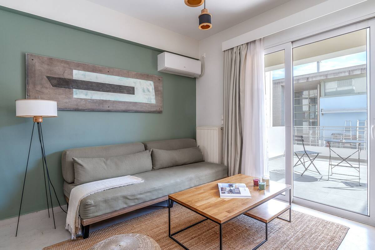 A modern living room with a sofa, a wooden coffee table, and a large window with a view of the outside.