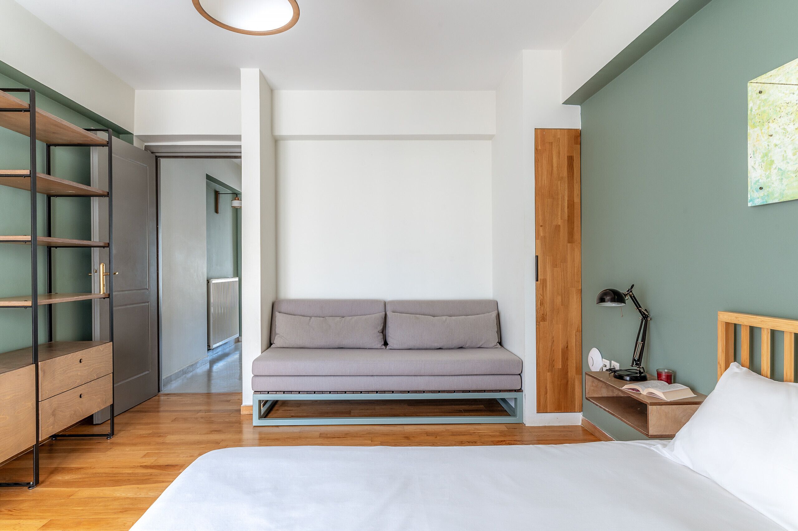 A modern bedroom with a bed, a grey sofa, a wooden nightstand, and a desk with a lamp.