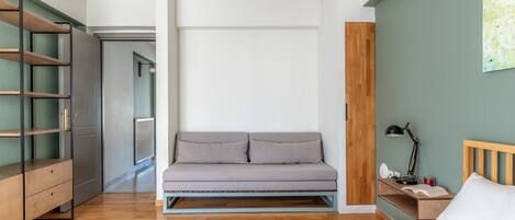 A modern bedroom with a bed, a grey sofa, a wooden nightstand, and a desk with a lamp.