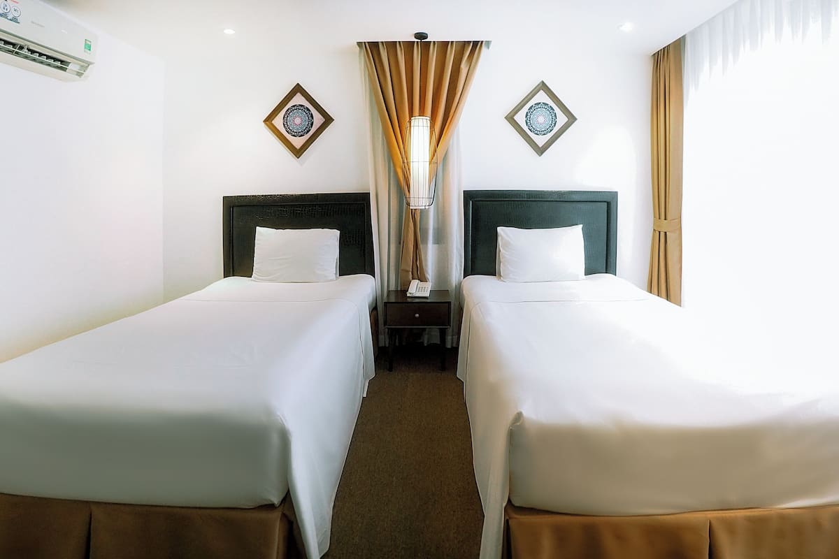 Une chambre d’hôtel avec deux lits simples, une table de chevet avec une lampe et un climatiseur fixé au mur.
