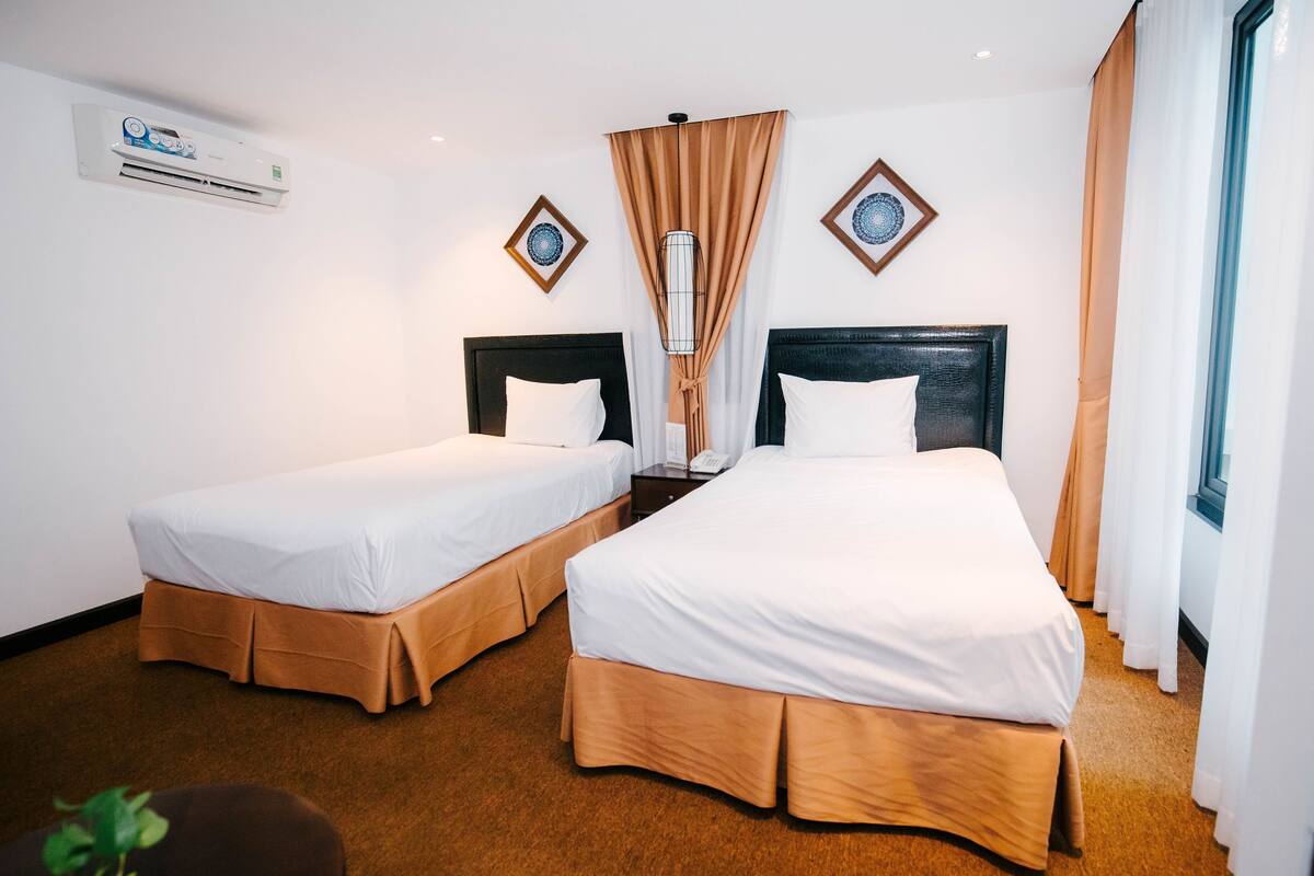 Une chambre d’hôtel avec deux lits, une table de chevet, un appareil de climatisation et une fenêtre avec des rideaux.