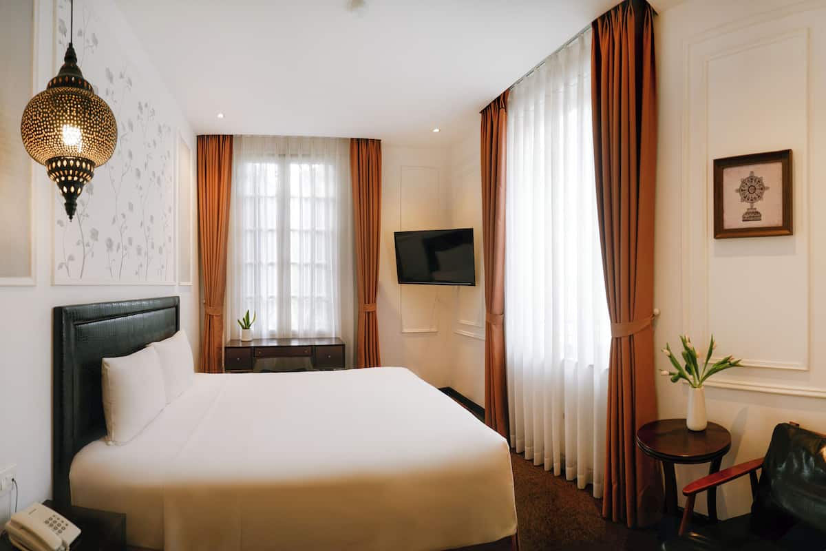 Une chambre d’hôtel avec un grand lit, un téléviseur à écran plat fixé au mur, une petite table ornée d’un vase de fleurs et une chaise.