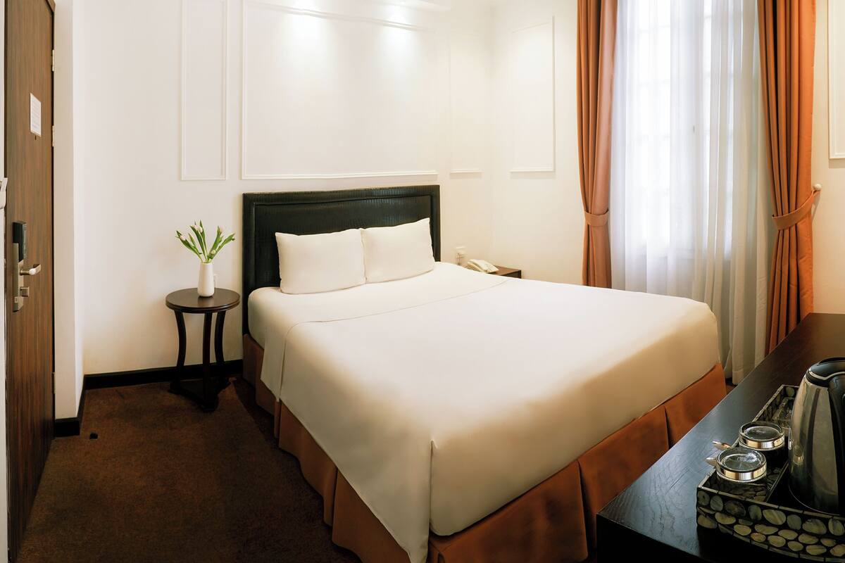 Une chambre d’hôtel avec un grand lit, une table de chevet avec une lampe, une petite plante en pot et une machine à café sur la table d’appoint.