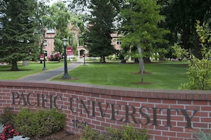 A brick wall with the text "PACIFIC UNIVERSITY" and a well-maintained lawn with trees and a building in the background. - Home2 Suites by Hilton Portland Hillsboro (Hillsboro)