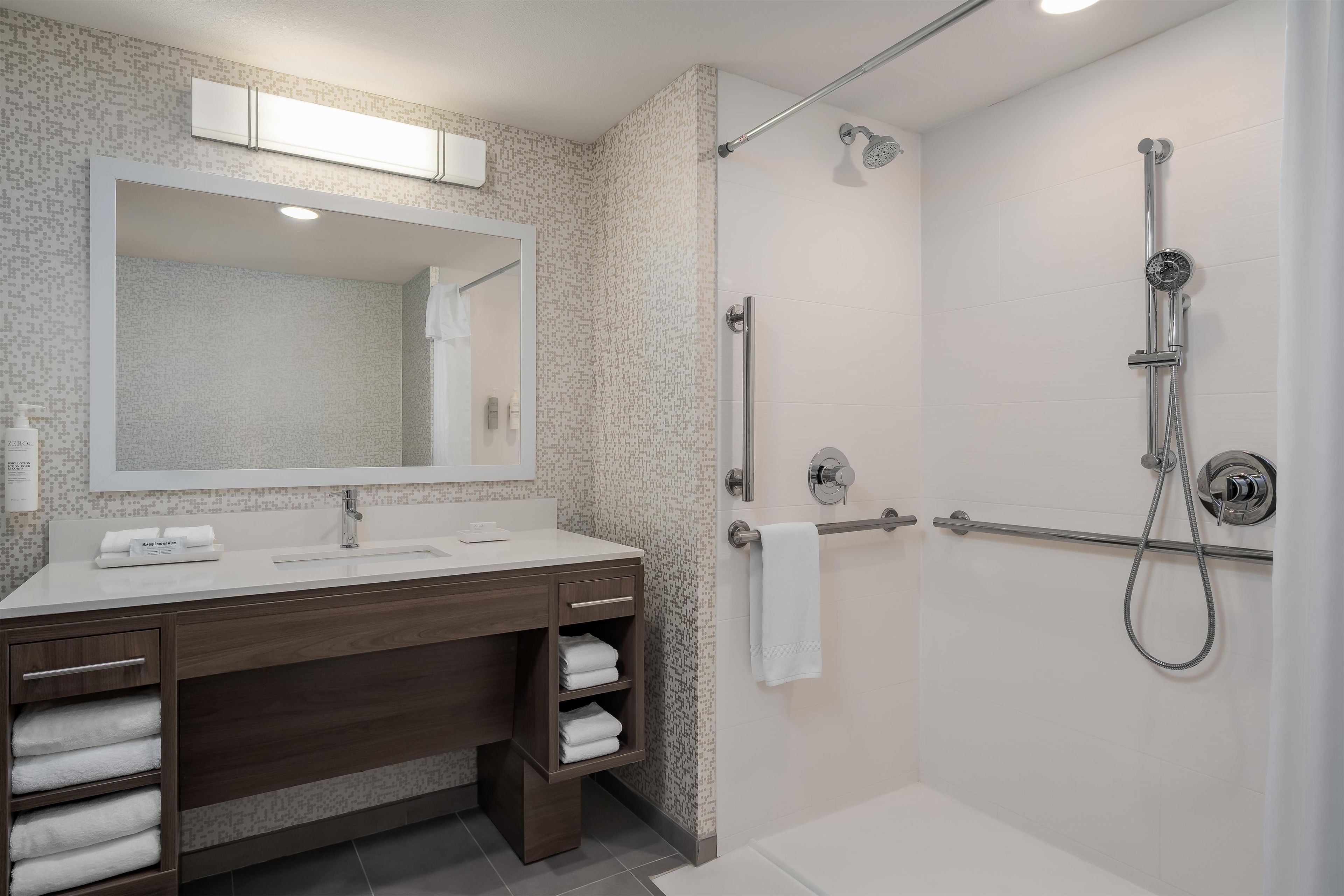Un baño moderno con ducha, lavabo con espejo y barra para toallas.