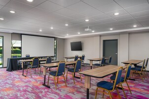 Un salón de conferencias con varias mesas y sillas, una pantalla de proyector y un ventanal grande.