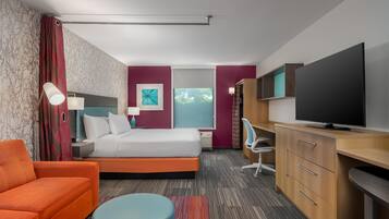 Habitación de hotel con cama, escritorio con televisor, silla y ventana con vistas.
