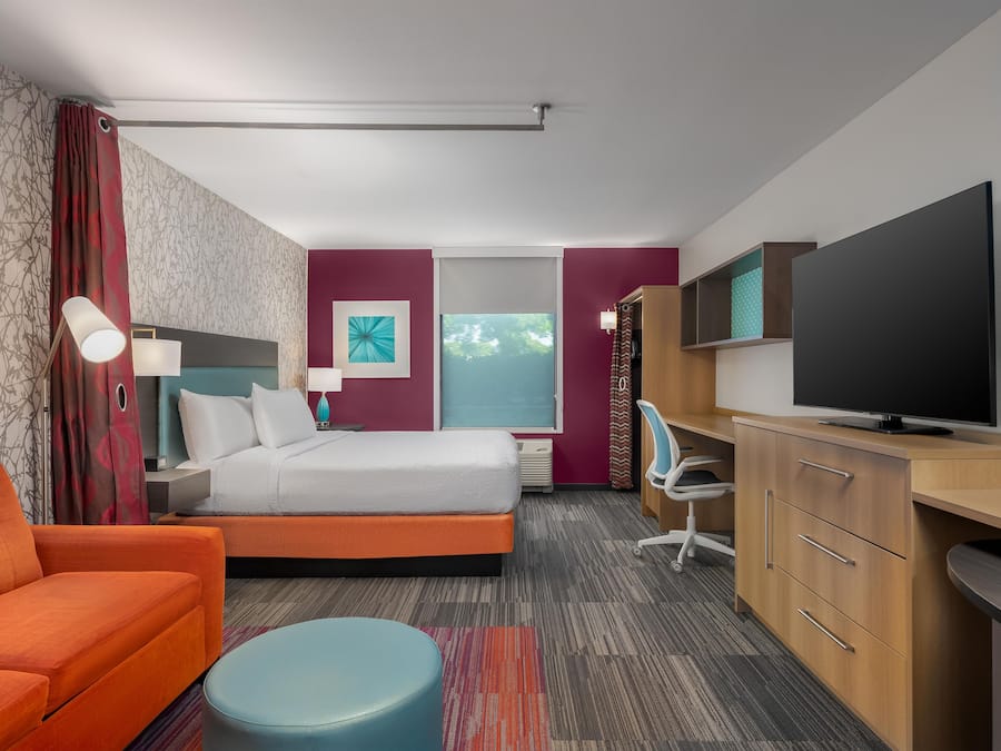 A hotel room with a bed, a desk with a television, a chair, and a window with a view.