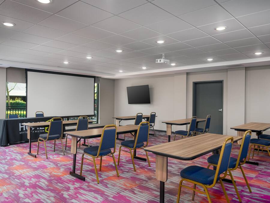 A conference room with multiple tables and chairs, a projector screen, and a large window.