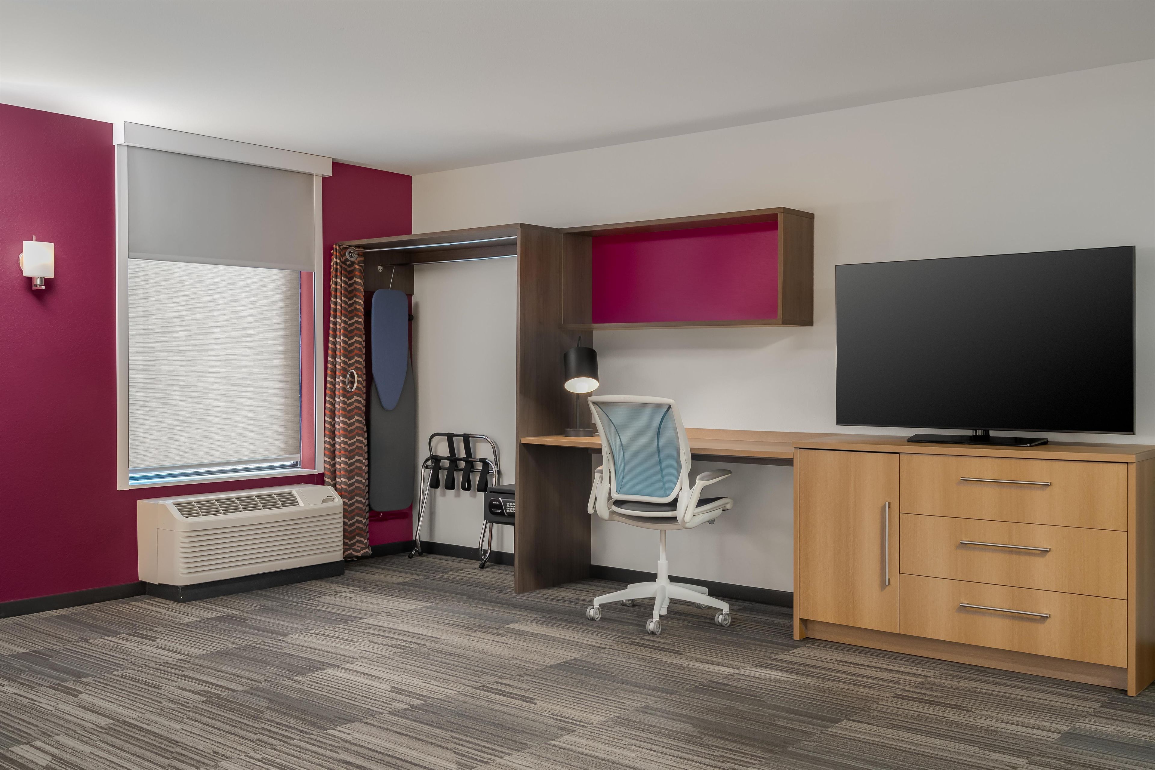 Habitación de hotel con cama, escritorio, silla, televisor, calentador y ventana con cortinas.