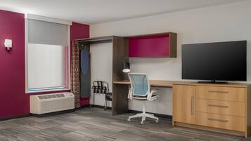 Habitación de hotel con cama, escritorio, silla, televisor, calentador y ventana con cortinas.