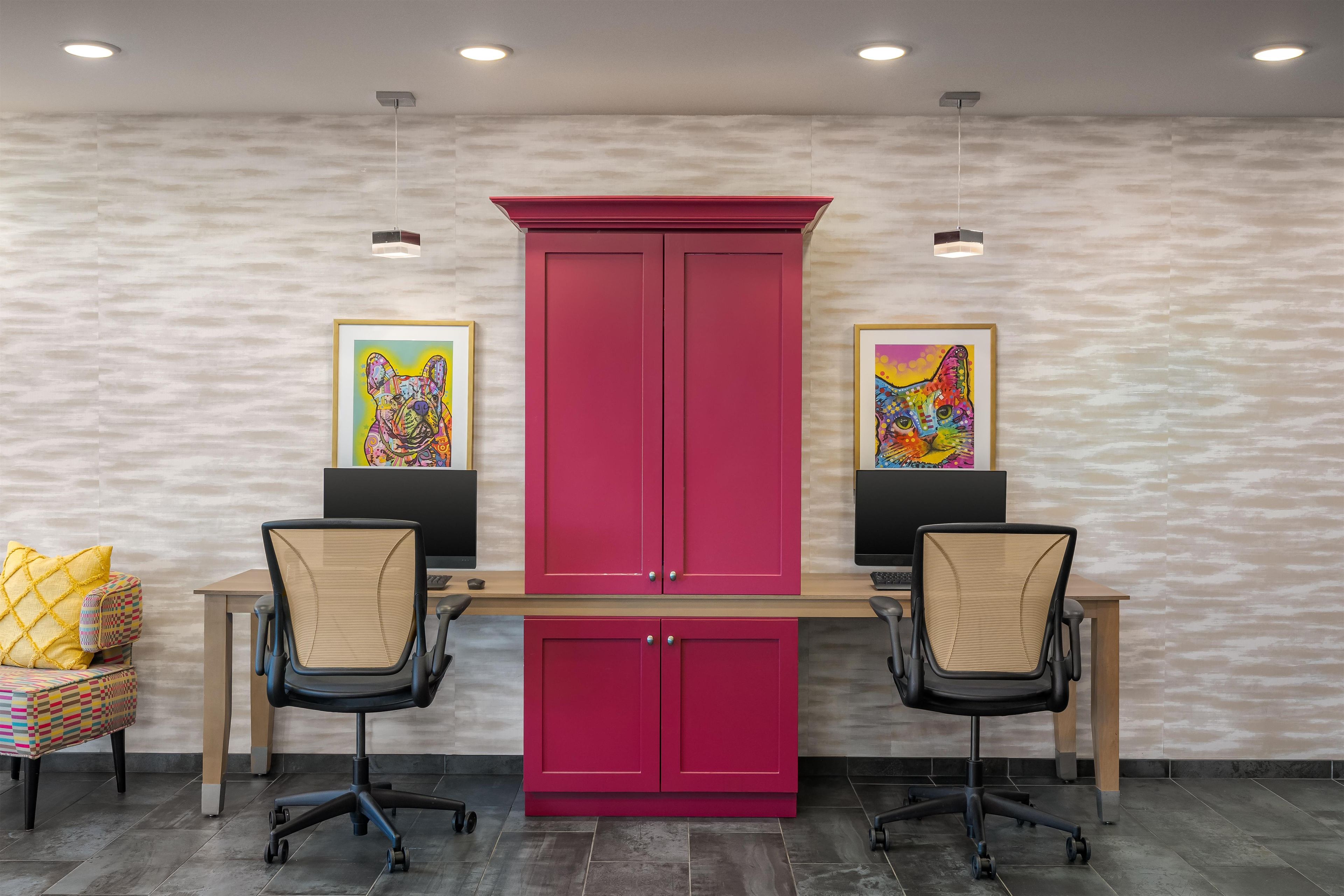 A conference room with two desks, chairs, a central cabinet, and two framed artworks on the wall.