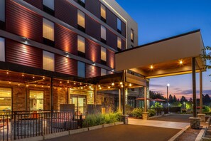 A hotel with a covered outdoor seating area, stone facade, and a view of the sky. - Home2 Suites by Hilton Portland Hillsboro (Hillsboro)