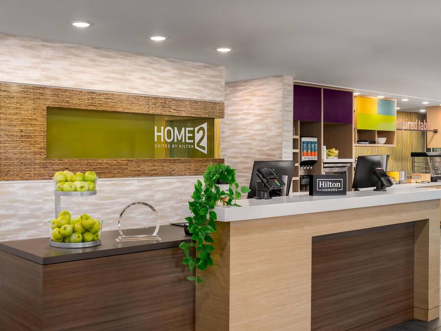 Un comptoir d’accueil d’hôtel avec un revêtement en bois, une vitrine en verre contenant des pommes et une enseigne indiquant « Hilton HONORS ».