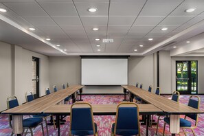 A conference room with a long table, chairs, a projector screen, and a patterned carpet. - Home2 Suites by Hilton Portland Hillsboro (Hillsboro)