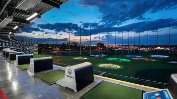 A golf driving range with multiple tee boxes and a well-lit driving area.
