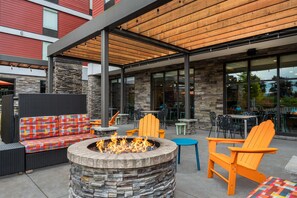 An outdoor seating area with a fire pit, wicker furniture, and stone walls. - Home2 Suites by Hilton Portland Hillsboro (Hillsboro)