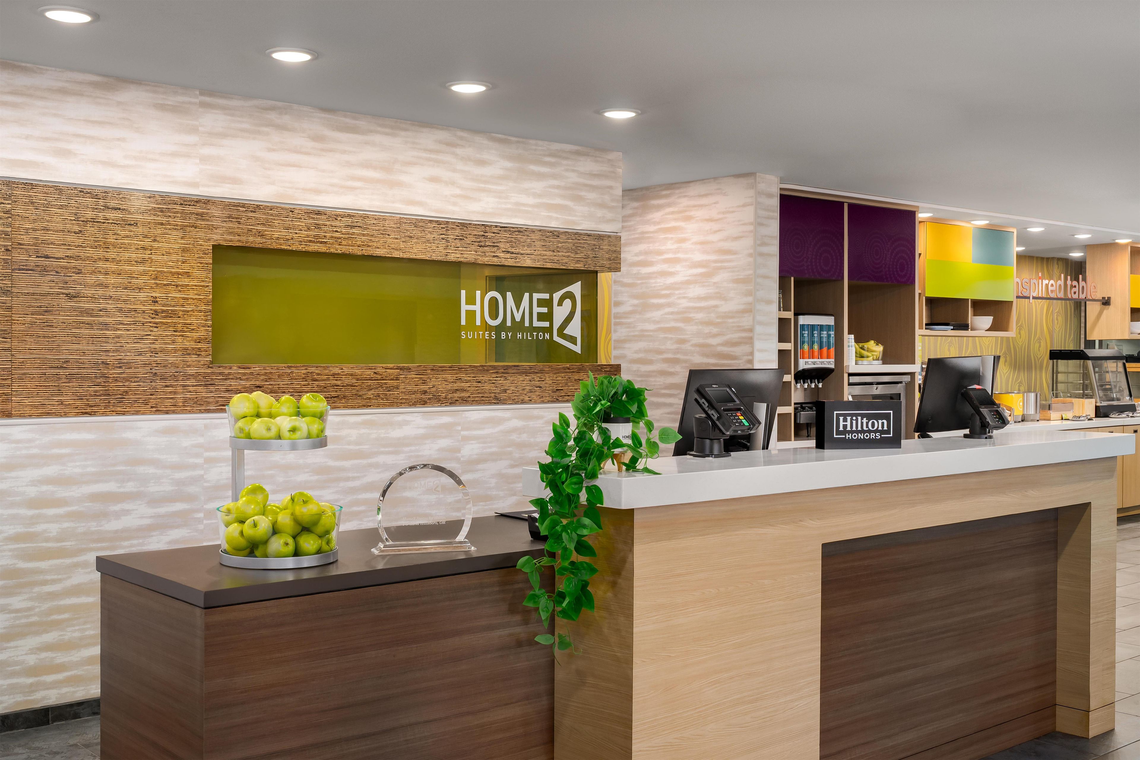 A hotel reception desk with a wooden finish, a glass display case with apples, and a sign reading 'Hilton HONORS'.