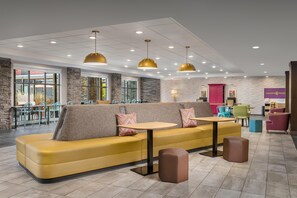 A modern lounge area with a yellow sofa, multiple tables, and pendant lighting. - Home2 Suites by Hilton Portland Hillsboro (Hillsboro)