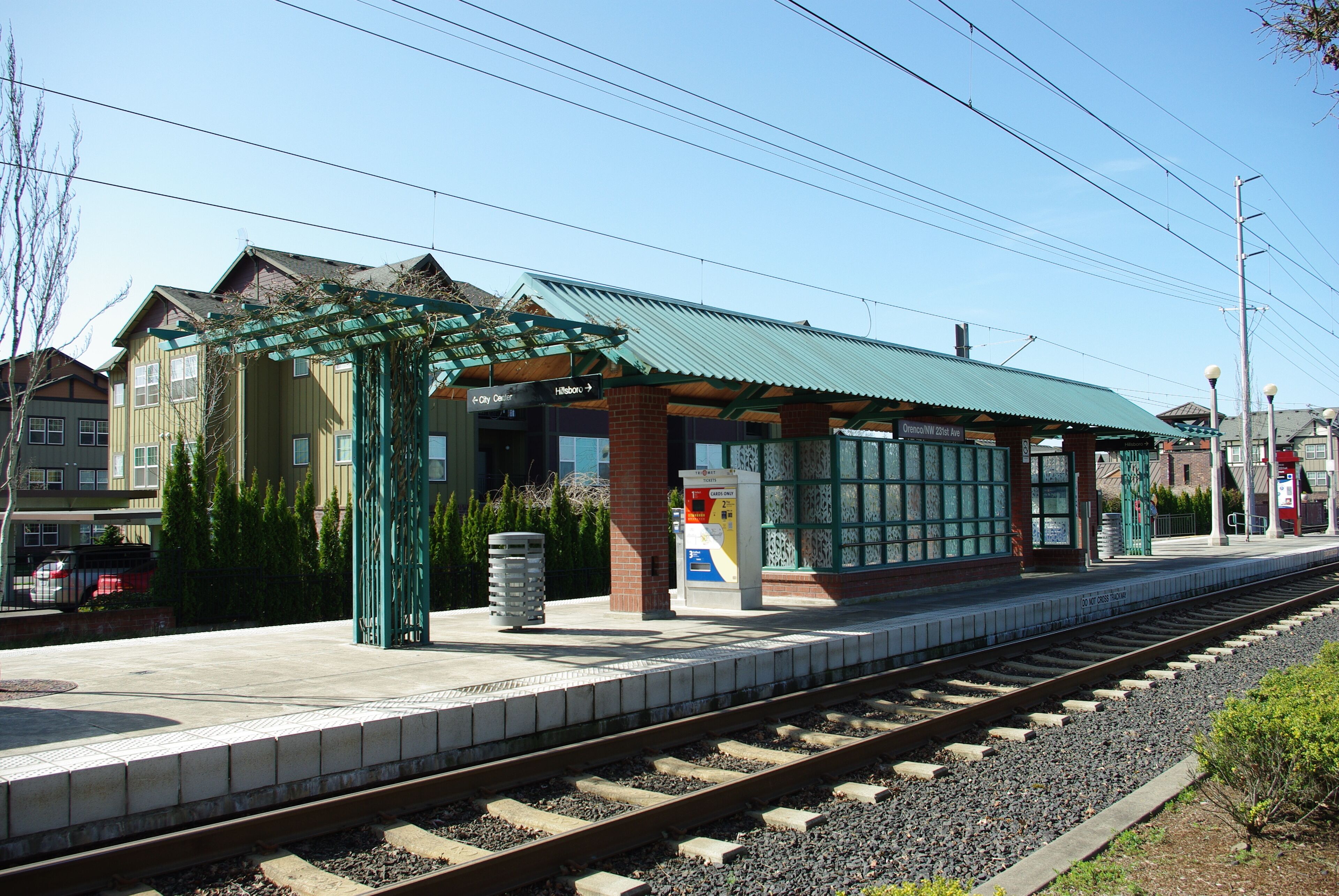 A train station platform with a green roof, a ticket machine, and a shelter.
