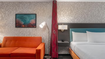 Ein Hotelzimmer mit Bett, Nachttisch, Lampe, Stuhl und einem Gemälde an der Wand.