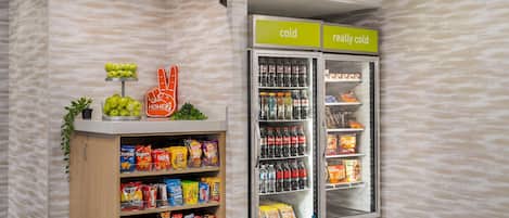 Un présentoir proposant divers types de chips et d’en-cas, un rayon réfrigéré contenant des boissons, et un panneau indiquant les sections « froid » et « très froid ».