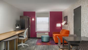 A compact hotel room with a desk, a television, a sofa, and a dining table.