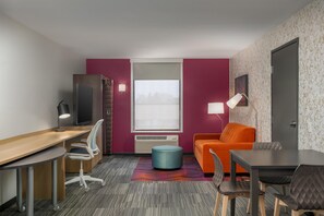 A compact hotel room with a desk, a television, a sofa, and a dining table. - Home2 Suites by Hilton Portland Hillsboro (Hillsboro)