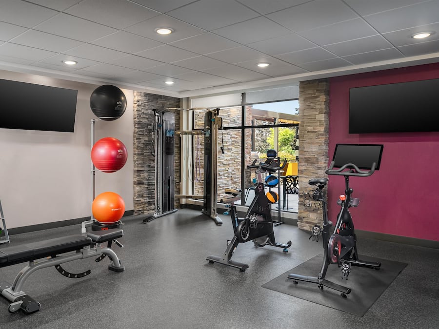 A gym with exercise equipment, a bench, kettlebells, and a wall-mounted TV.