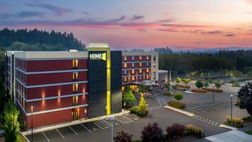 A hotel with a modern design, featuring a prominent 'HOME 2' sign, a parking lot, and a landscaped area with trees and shrubs.