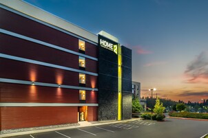 Un moderno edificio de hotel con un llamativo letrero 'HOME 2', varias ventanas y un estacionamiento.