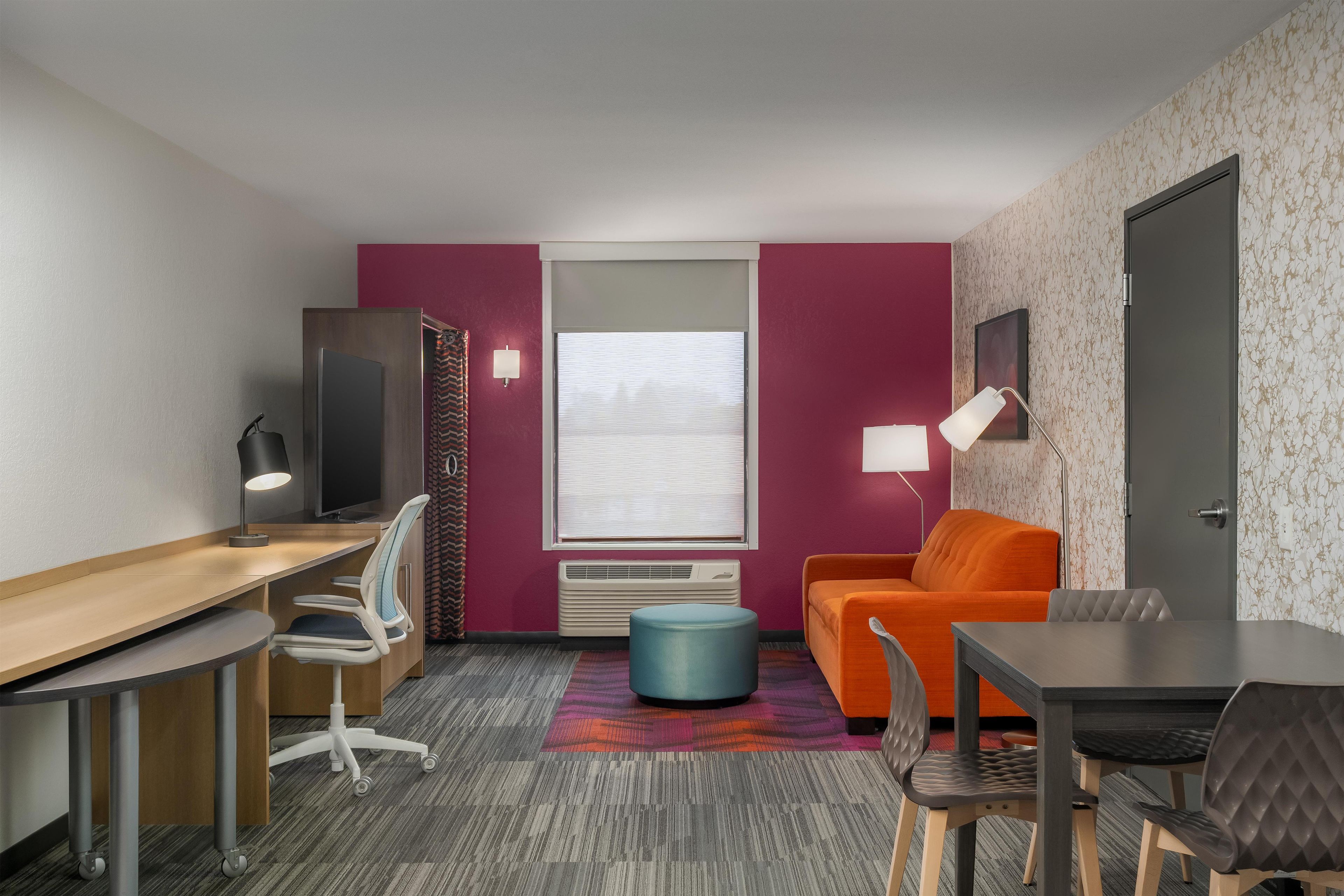 Habitación de hotel compacta con escritorio, televisor, sofá y mesa de comedor.