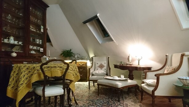 A dining area with a high ceiling, a wooden cabinet with glass doors, a patterned tablecloth-covered table, and a traditional rug.