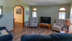 Ein Wohnzimmer mit Fernseher, zwei Sesseln, einer Couch und einem Couchtisch aus Holz.