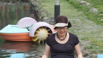 A person in a yellow boat on a calm water body with a stone pathway and potted plants in the background.
