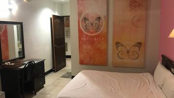 Habitación de hotel con cama, escritorio con silla y dos cuadros decorativos con temática de mariposas.