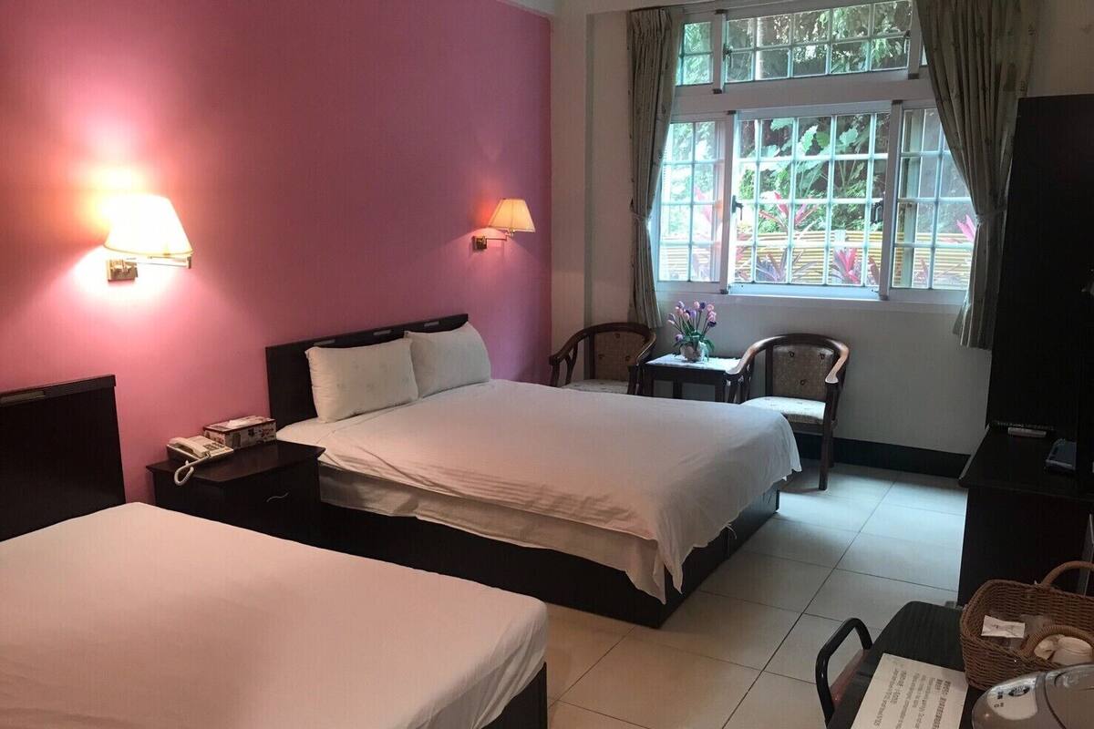 A hotel room with two beds, a desk, a chair, and a window with curtains.
