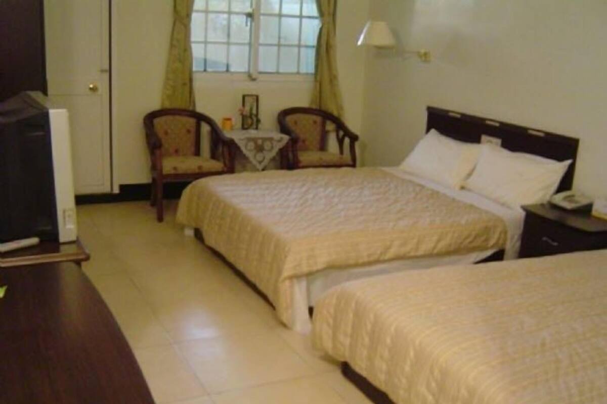 A hotel room with two beds, a desk, a chair, a small table, and a window with curtains.