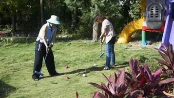 Two people playing golf on a grassy field with trees in the background.