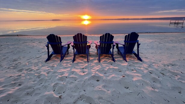 Four Adirondack chairs facing a sunset over a calm body of water. - Summer Sand & Fun Beachfront Vacation Traverse City In Cottage (Traverse City)