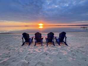 Fire Adirondack-stole vender sig mod en solnedgang over stille vand.
