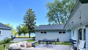 A deck with outdoor furniture, a view of the ocean, and a house with a white exterior. - Summer Sand & Fun Beachfront Vacation Traverse City In Cottage (Traverse City)
